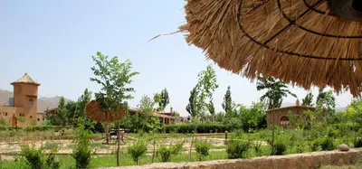 a garden with a building and a straw umbrella at AZIGHAME Complexe Touristique in Tinerhir