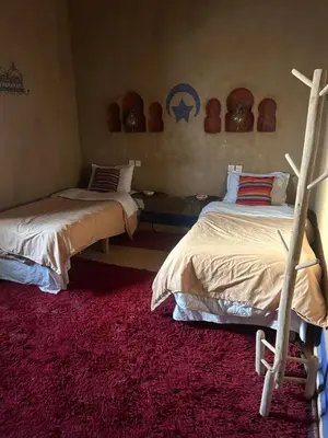 a bedroom with two beds and a red rug at kasbah planet sahara in Merzouga