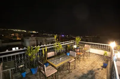 a patio with tables and chairs on a balcony at night at Riad Dar Rabha in Fès