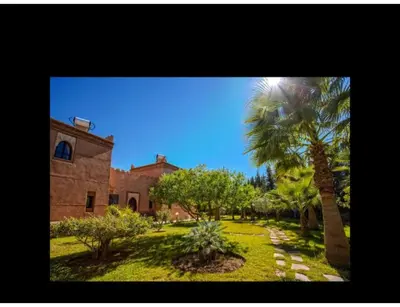 a building with a palm tree in front of a yard at Palace with 2 villas and 2 swimming pools in Sidi Abdellah Ghiat in Had Abdallah Rhiat