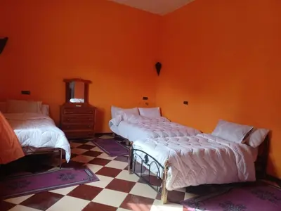 two beds in a room with an orange wall at Riad gnaoua khamlia in Merzouga