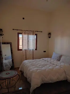 a bedroom with a bed and a table and a window at Riad gnaoua khamlia in Merzouga