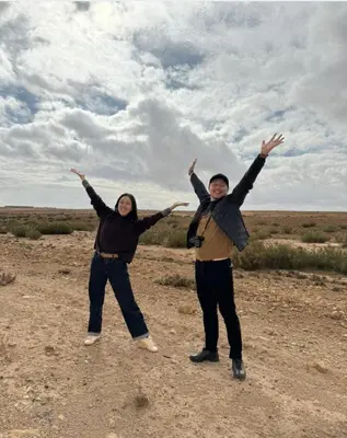 two people standing in a field with their arms in the air at Abdo Luxury Camp with Heating in Merzouga
