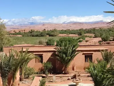 a house in the desert with palm trees and mountains at Maison d'hôtes Tigminou - Adults Only in Aït Ben Haddou
