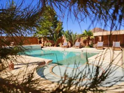 a swimming pool with chairs and palm trees at Maison d'hôtes Tigminou - Adults Only in Aït Ben Haddou
