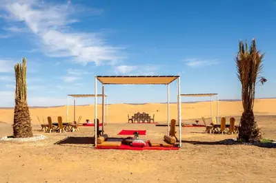 a tent in the desert with chairs and palm trees at LEMNAOUAR ERG CAMP in Merzouga