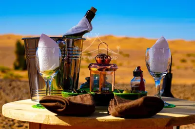 a table with two glasses and a bottle of wine at The White Camp Merzouga - Official Luxury Desert Camp & Camel Tours in Merzouga