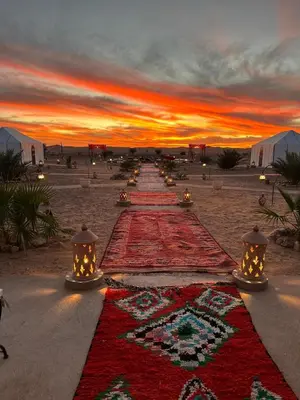 a long row of carpets on the beach at sunset at The White Camp Merzouga - Official Luxury Desert Camp & Camel Tours in Merzouga