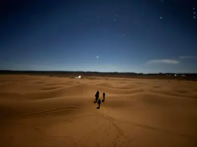 two people walking through a desert at night at Mhamid Sahara Camp - Mhamid El Ghizlane in Mhamid