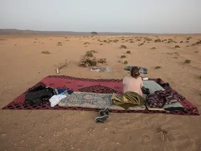 a woman sitting on a blanket in the desert at Mhamid Sahara Camp - Mhamid El Ghizlane in Mhamid