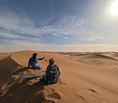 two people sitting on the sand in the desert at Mhamid Sahara Camp - Mhamid El Ghizlane in Mhamid