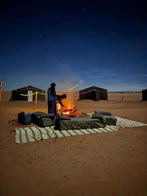 a man standing next to a fire in the desert at Mhamid Sahara Camp - Mhamid El Ghizlane in Mhamid