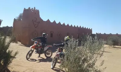 two people on dirt bikes in front of a building at Auberge Dinosaur Kem Kem in Tafraoute Sidi Ali