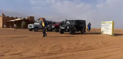 a man standing in front of two jeepneys in the desert at Auberge Dinosaur Kem Kem in Tafraoute Sidi Ali