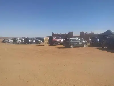 a group of cars parked in a dirt parking lot at Auberge Dinosaur Kem Kem in Tafraoute Sidi Ali