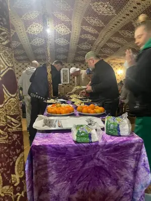 a group of people standing around a table with oranges at Merzouga Camel Trekking Camp in Merzouga