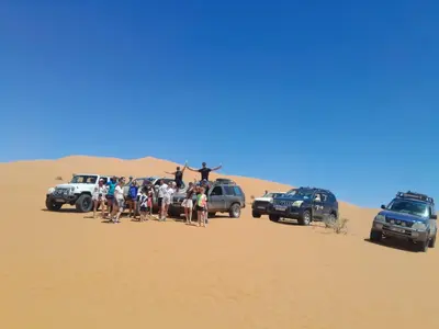 a group of people standing in the sand in the desert at Merzouga Camel Trekking Camp in Merzouga