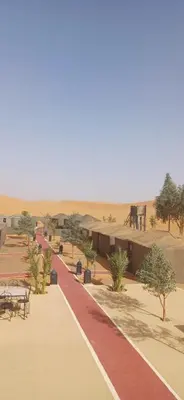 a walkway in the desert with tables and benches at Merzouga Camel Trekking Camp in Merzouga