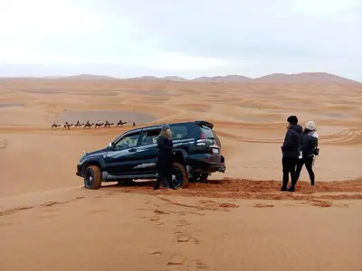 a group of people standing around a suv in the desert at Merzouga Ana luxury Camp in Merzouga