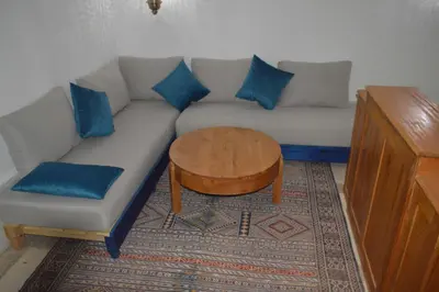 a living room with a couch with blue pillows and a table at Riad Tin Hinane in Merzouga