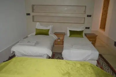 two twin beds in a room with green sheets at Riad Tin Hinane in Merzouga