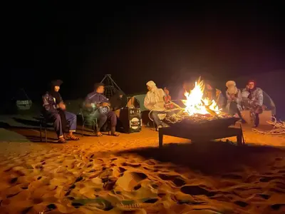a group of people sitting around a fire at night at Aladdin Desert Lodge - Mhamid Sahara Camp in El Gouera