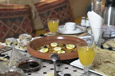 a table with a bowl of food and glasses of orange juice at Aladdin Desert Lodge - Mhamid Sahara Camp in El Gouera