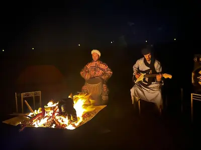 a group of three people standing around a fire at Aladdin Desert Lodge - Mhamid Sahara Camp in El Gouera