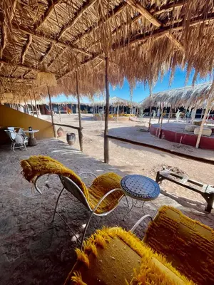 a beach with a table and chairs and a straw umbrella at Aladdin Desert Lodge - Mhamid Sahara Camp in El Gouera