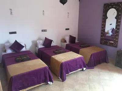 three beds in a room with purple sheets at Riad Moha in Merzouga
