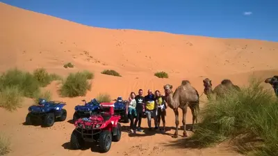 a group of people standing in the desert with atvs and a camel at Riad Moha in Merzouga
