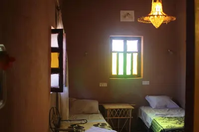 a room with two beds and a window and a chandelier at auberge restau tombouctou in Aït Ben Haddou