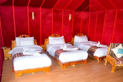 three beds in a room with a red wall at Relaxing Desert Camp in Merzouga