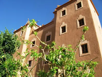 a tall building with trees in front of it at Casbah d'hôte La Jeanne Tourisme Ecologique in Boumalne