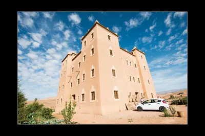 a white car parked in front of a large building at Casbah d'hôte La Jeanne Tourisme Ecologique in Boumalne