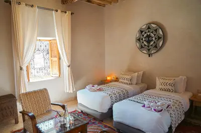 a room with two beds and a chair and a window at Kasbah Hnini in Igdourane