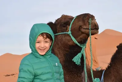 a young boy standing next to a camel in the desert at Moda Camp merzouga tours Quad Sunboarding ATV in Merzouga