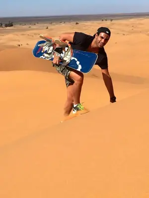 a man holding a skateboard in the desert at Moda Camp merzouga tours Quad Sunboarding ATV in Merzouga