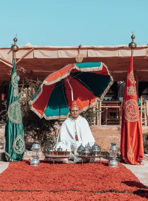 a man is sitting under an umbrella with food at Imperial Glory Lodges in Merzouga