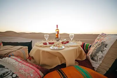 a table in the middle of the desert with a bottle and glasses at Ghazala Camp - Luxury Erg Chigaga Magic in Mhamid