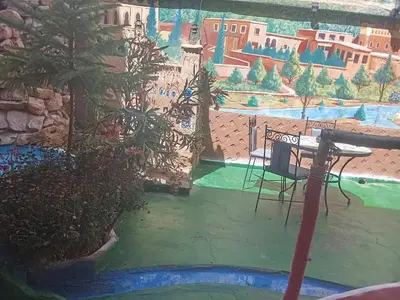a table and a chair in a garden with a painting at kasbah amlal in Boumalne