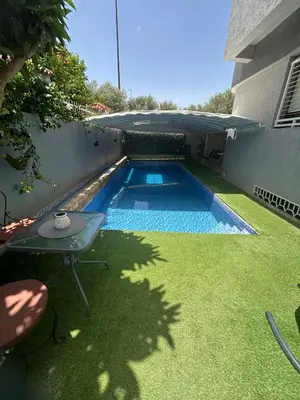 a small swimming pool with a table and grass at Dar el kebira in Meknès