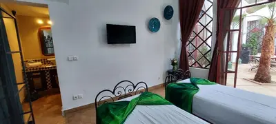 two beds in a room with a tv on the wall at Riad Ramzi in Marrakech