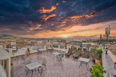 a rooftop patio with tables and chairs and a sunset at Riad Dari Fes in Fès