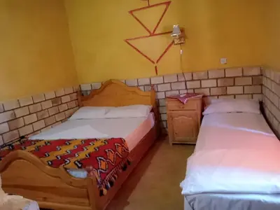 a room with two beds and a night stand at Les Pyramides Hotel Merzouga in Merzouga