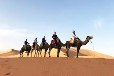 a group of people riding on camels in the desert at Les Pyramides Hotel Merzouga in Merzouga