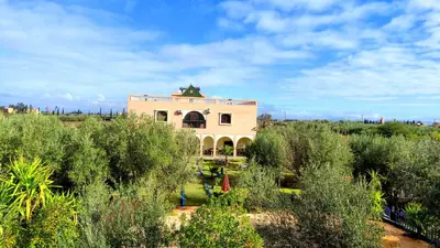a building in the middle of a field with trees at Guest House Qodwa in Marrakech