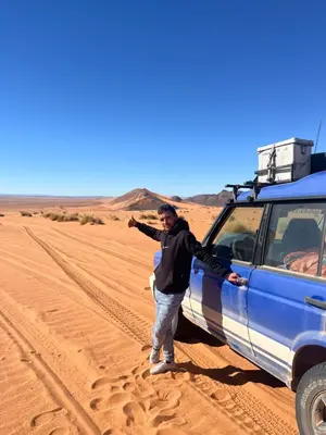 a man standing next to a blue truck in the desert at Maggaman Guest House in Tafraoute Sidi Ali