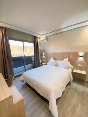 a bedroom with a white bed and a large window at HOTEL CAFE PALAIS SALAM , Beni Mellal in Beni Mellal