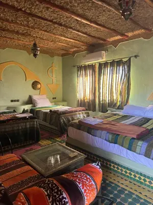 a room with three beds and a table in it at Hotel ksar merzouga in Merzouga